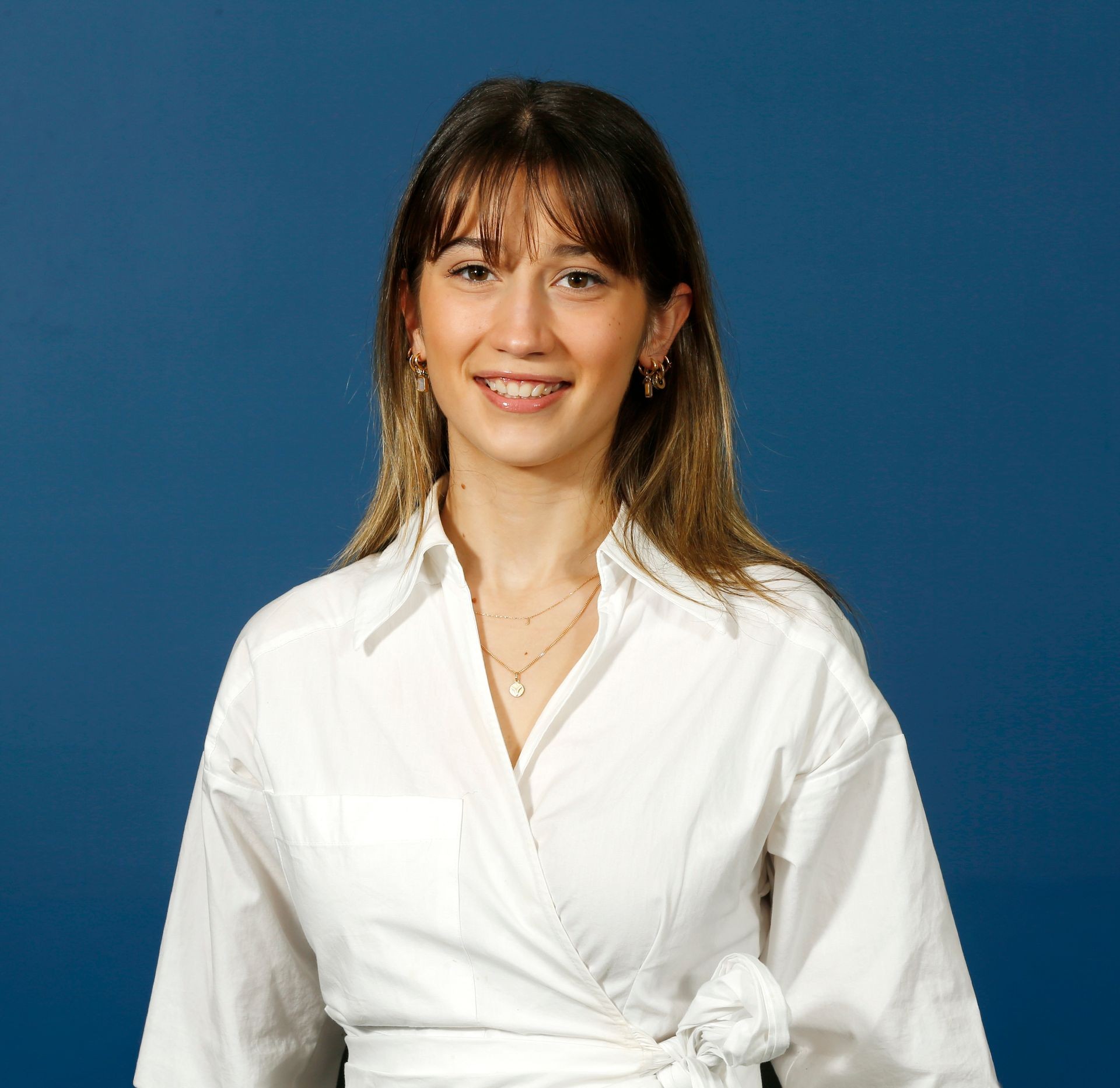 Smiling person in a white shirt standing against a blue background.