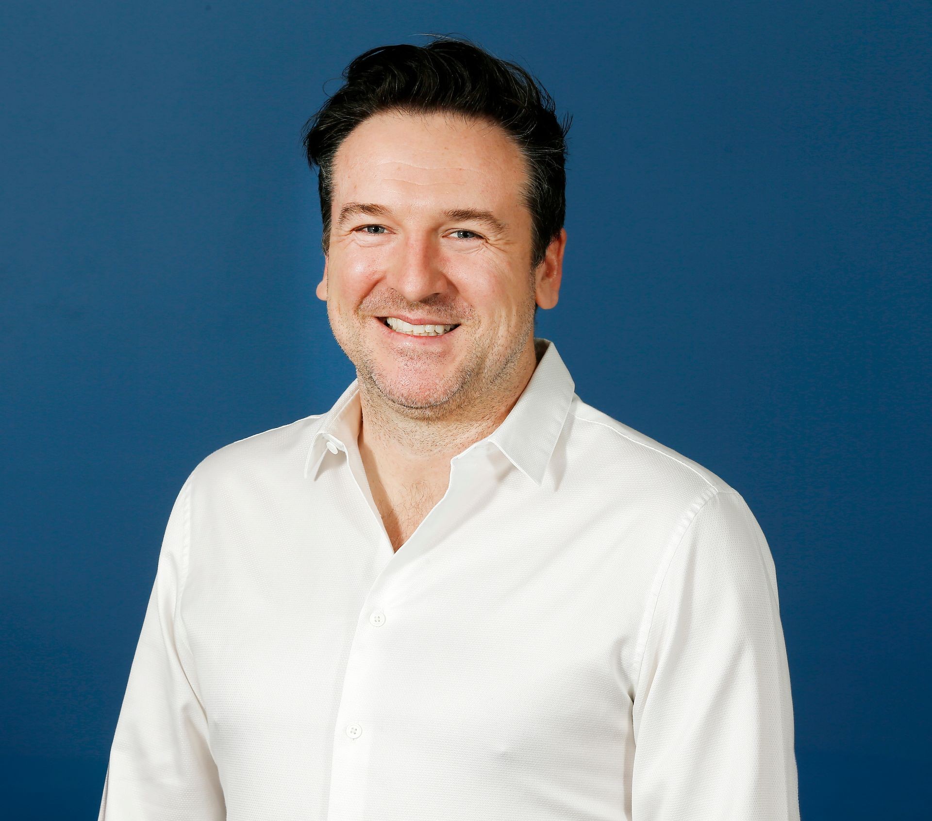 Person wearing a white dress shirt against a blue background.