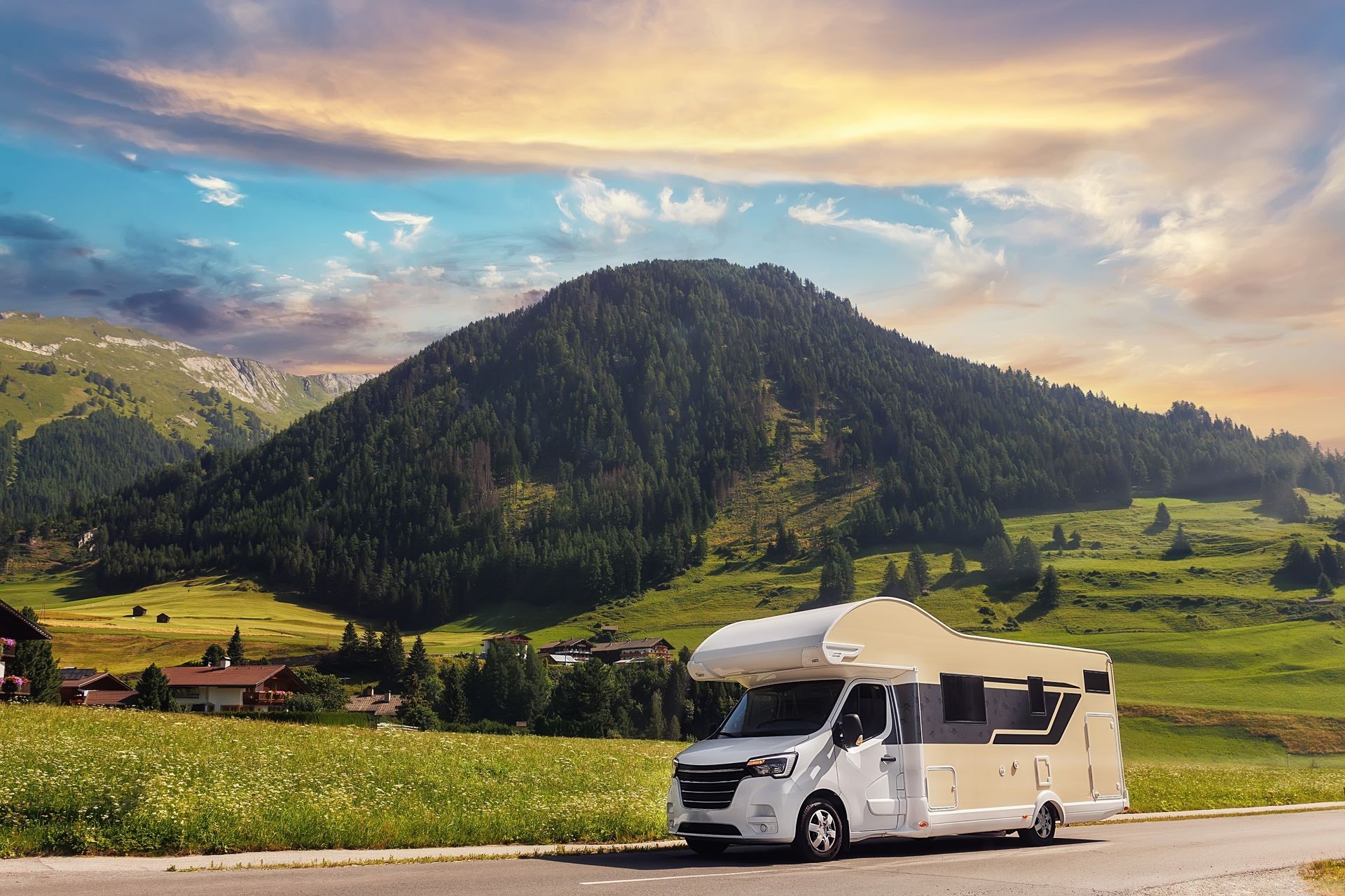 Motorhome parked on a road with scenic mountain and hillside view under a colorful sky.
