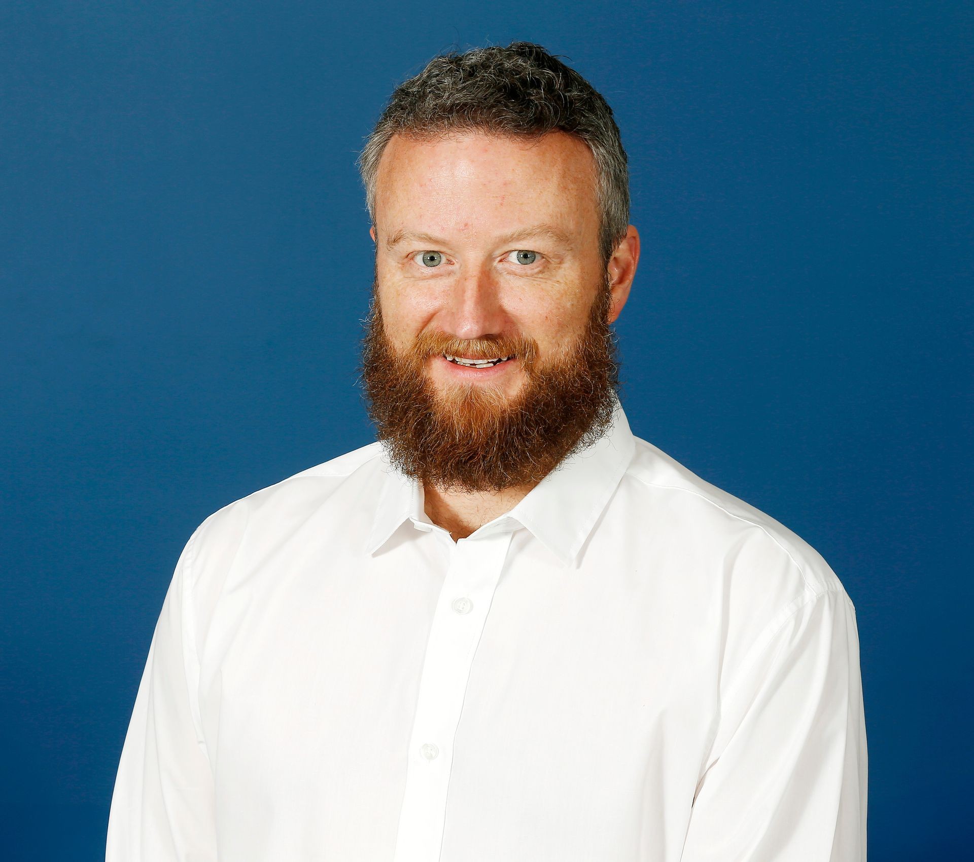 Man with a beard wearing a white shirt against a blue background.