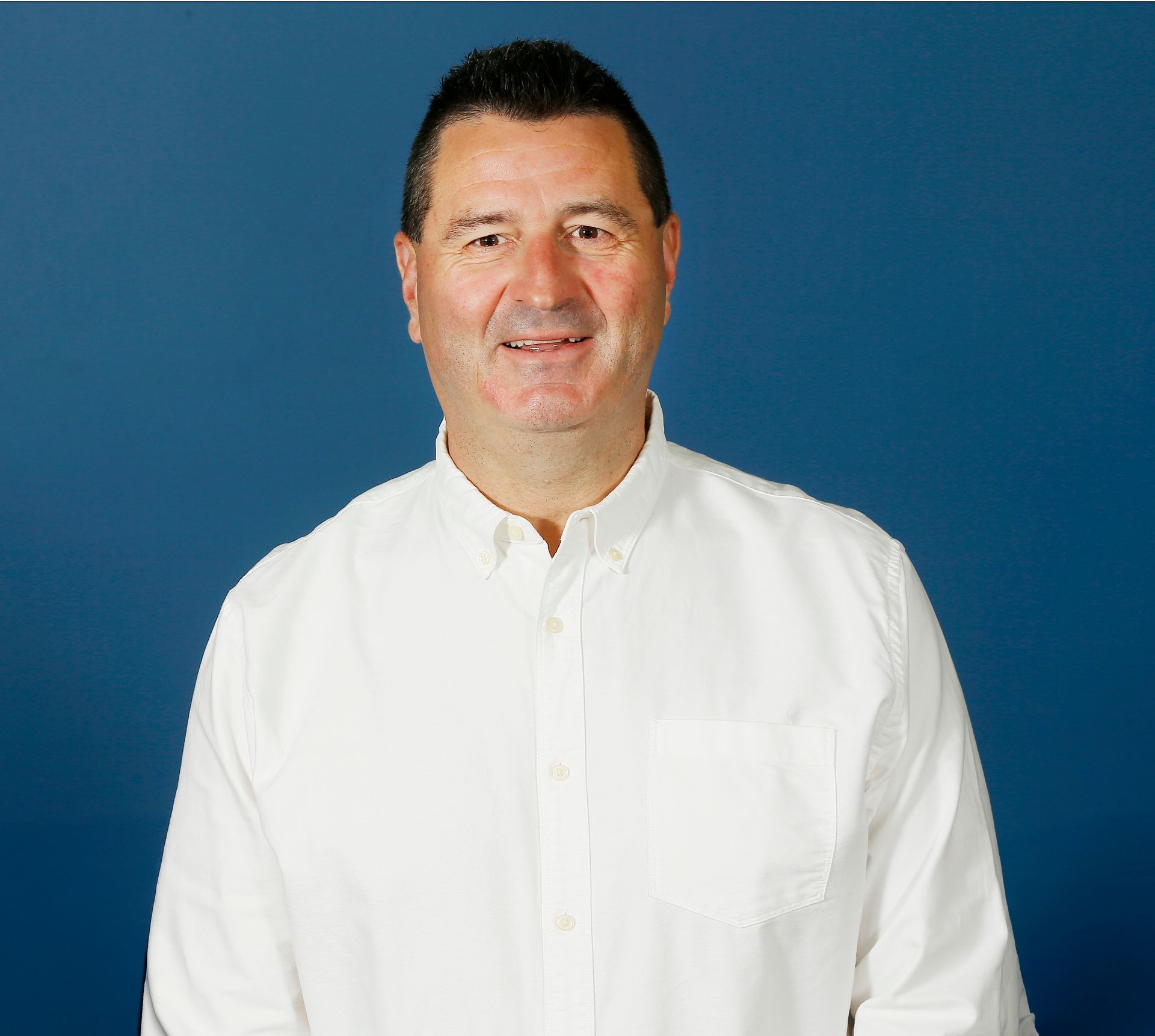 Smiling person wearing a white shirt standing against a blue background.