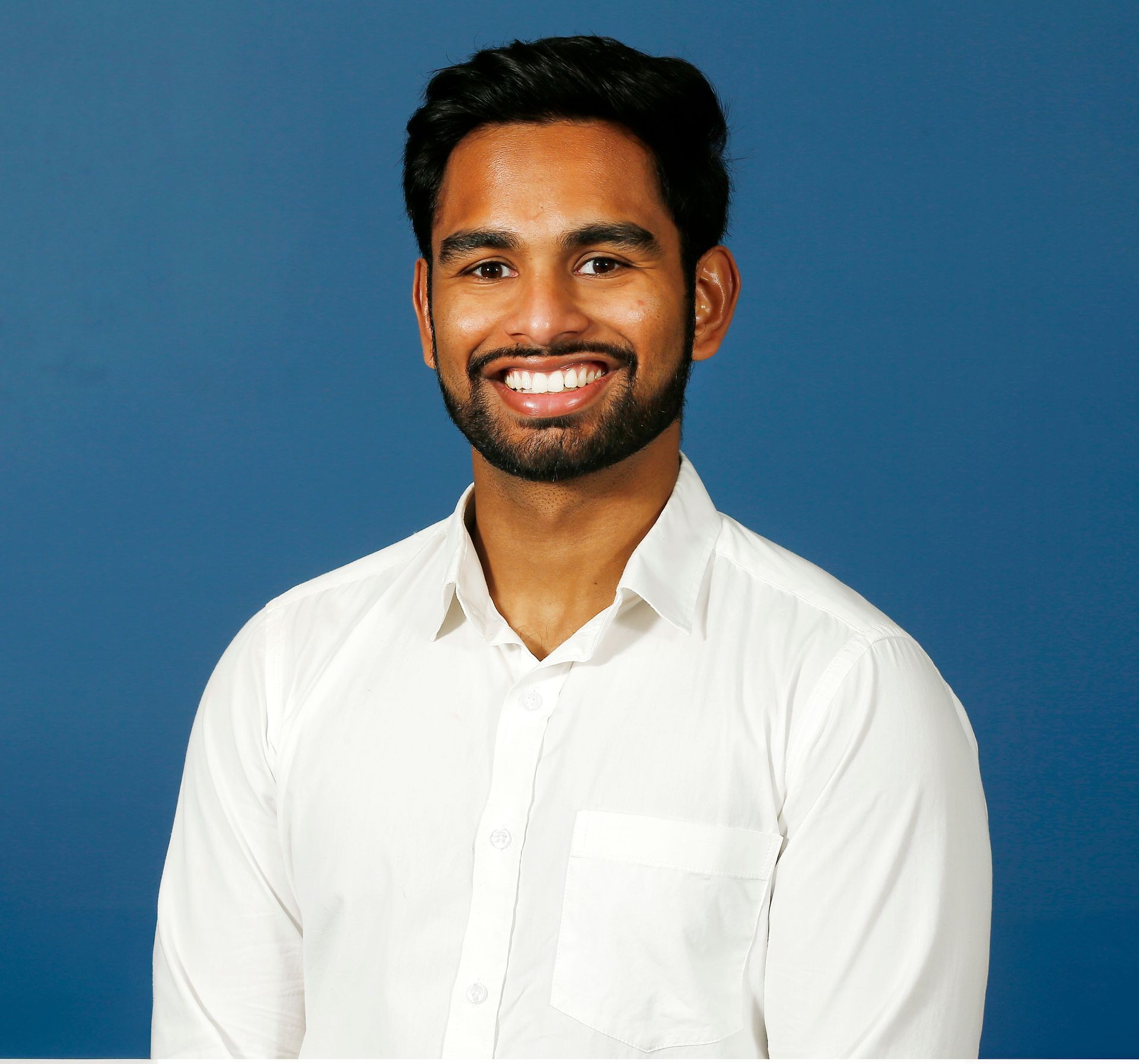 Smiling man in a white shirt against a blue background.