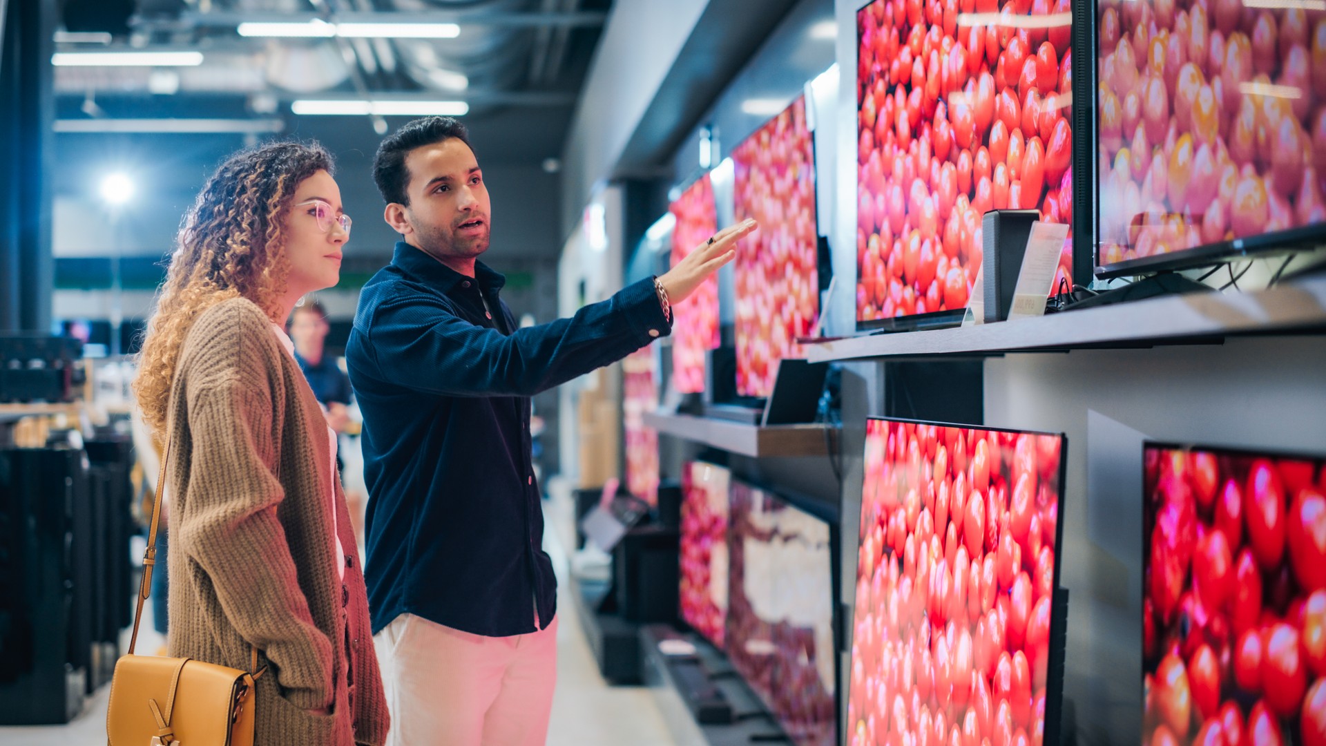 Stylish Multiethnic Couple is TV Shopping at Retail Electronics Store. Man and Female Seeking Sleek Flat-Screen TV for Their Home. Customers Deliberate Over Television Options in Contemporary Shop